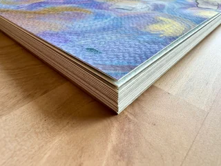 The corner of a handmade notebook with a blue and gold painted cover and a thick stack of white pages