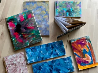 A group of colorful painted notebooks with one book fanned open to show its different papers