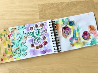 An open sketchbook filled with small drawings and watercolor studies across two white pages