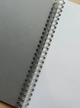 Grey sketch paper and textured white paper facing each other across silver binding