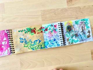 An extended sketchbook spread with colorful drawings and painted studies across brown and white papers