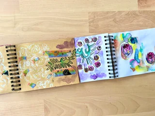 An open notebook with looping drawings on kraft paper beside colorful marks on white paper