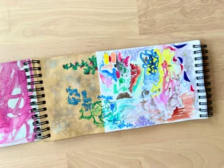 Separate notebook sections open to colorful drawings and paintings on brown and white paper