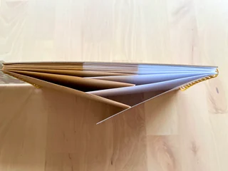 An open notebook viewed from the end, with kraft and white pages fanning out from their bindings