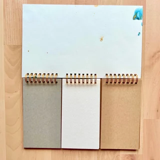 Three narrow notebook sections side by side, with gray, white, and kraft paper